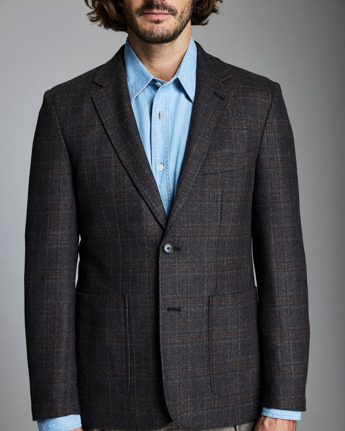 Man wearing a brown checkered blazer over a light blue shirt on a gray background