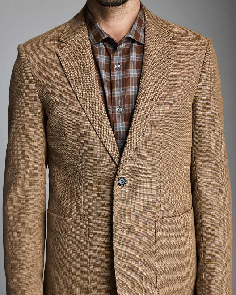 Brown blazer over a plaid shirt on a gray background