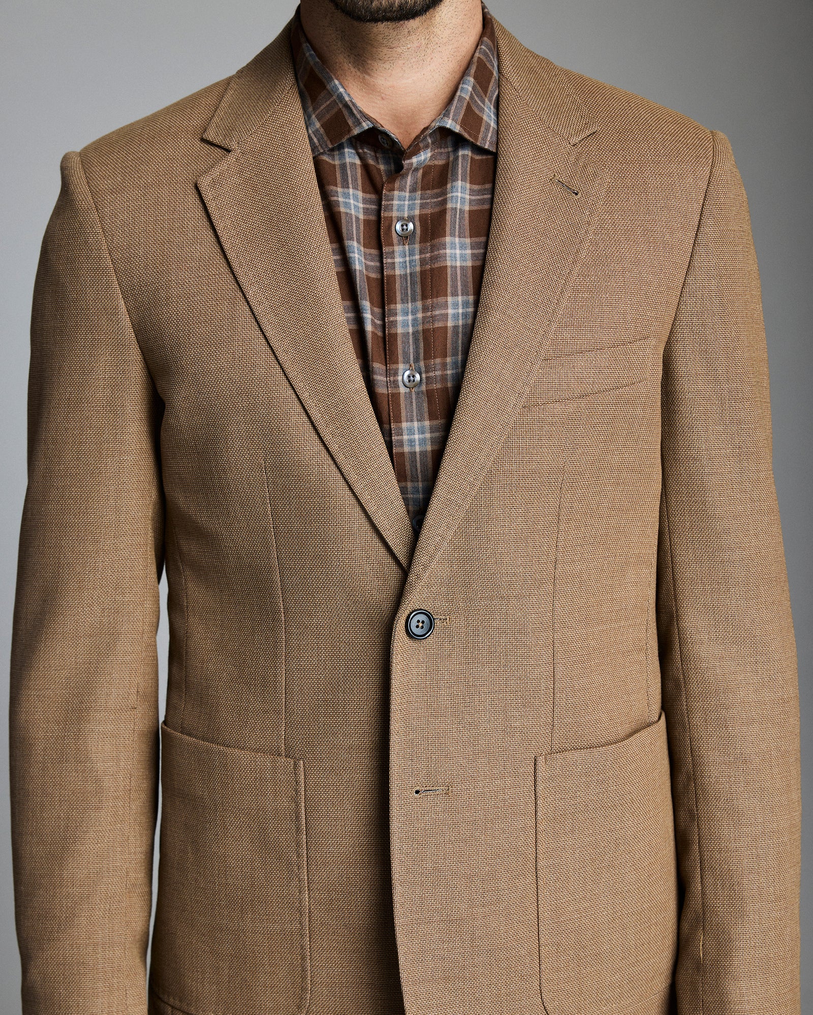 Brown blazer over a plaid shirt on a gray background