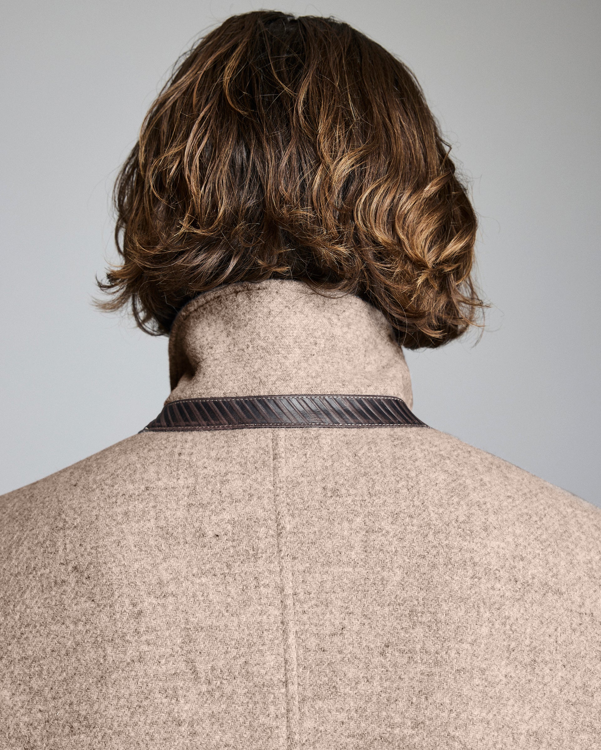 Back view of a person wearing a beige coat with a plain background