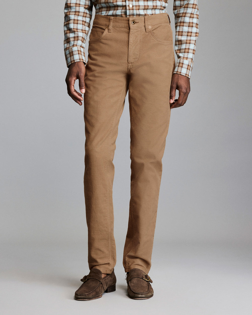 Person wearing brown pants and a plaid shirt on a plain background