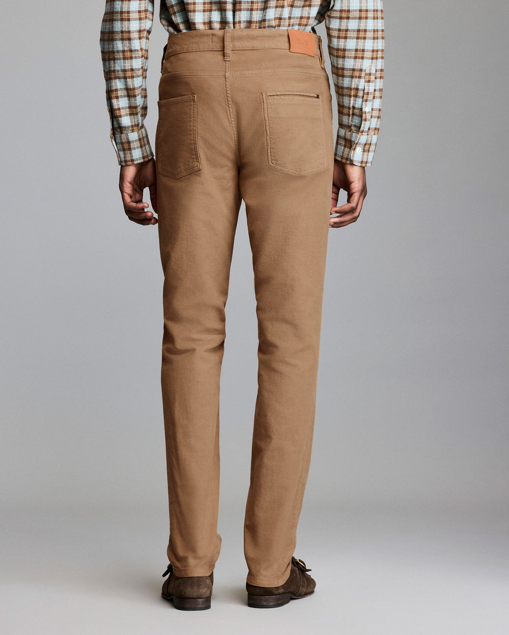 Person wearing brown pants with a plaid shirt on a gray background