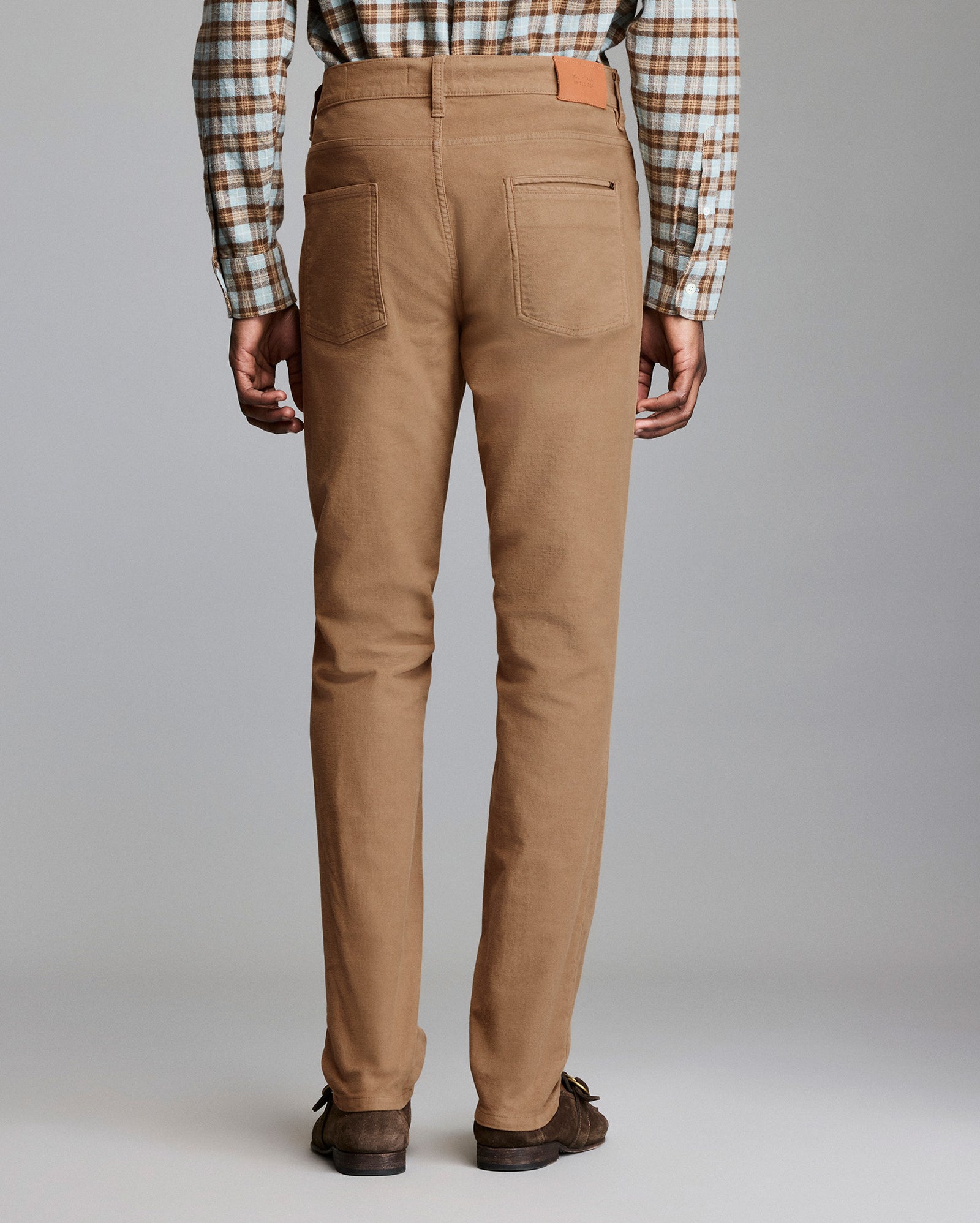 Person wearing brown pants with a plaid shirt on a gray background