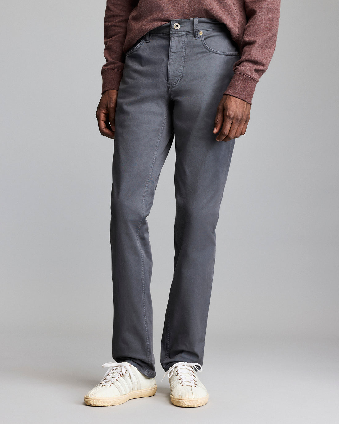 A person wearing a maroon sweater, gray pants, and white sneakers stands against a plain gray background. Only the lower half of their body is visible.