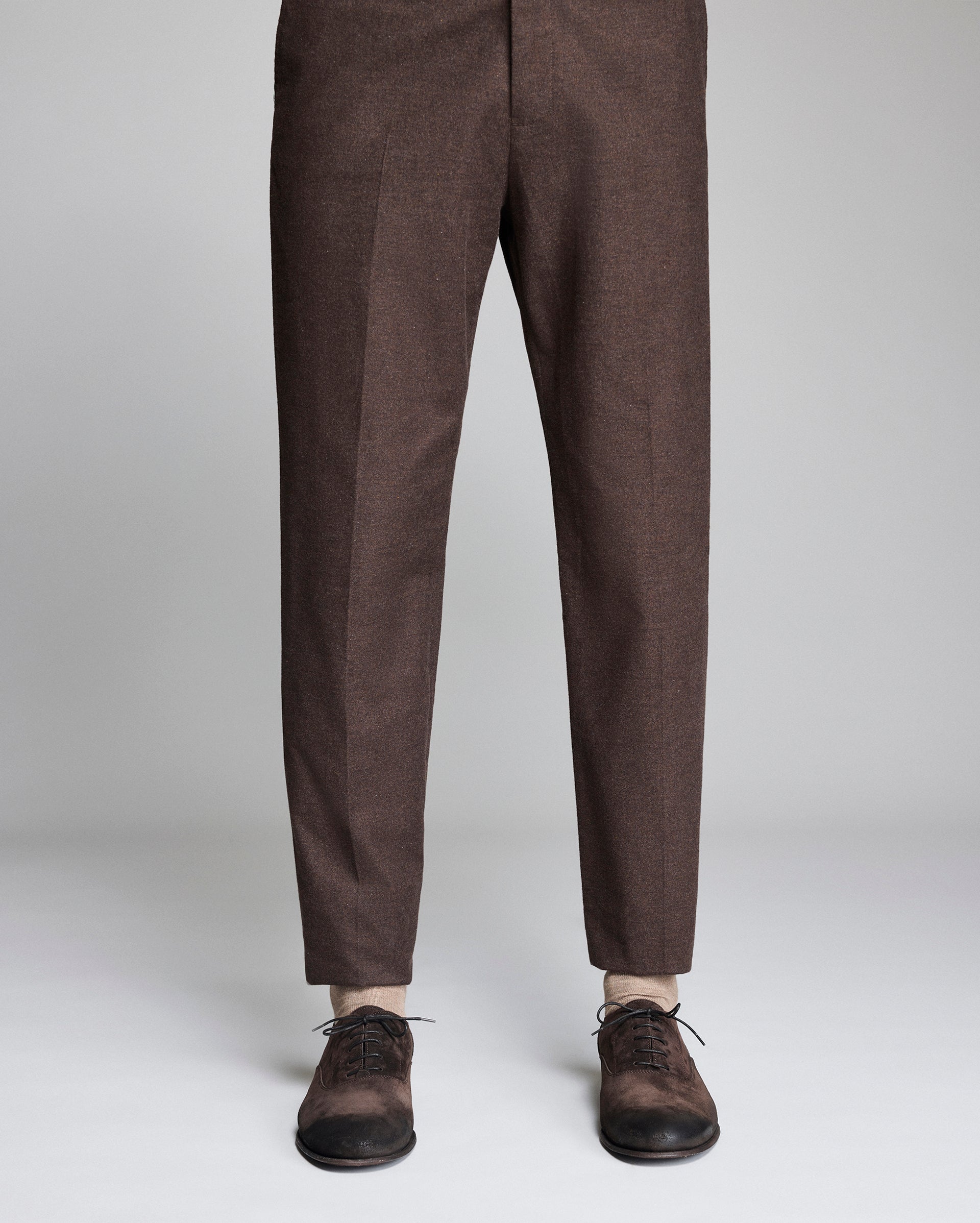 Brown pants worn with brown shoes on a light gray background