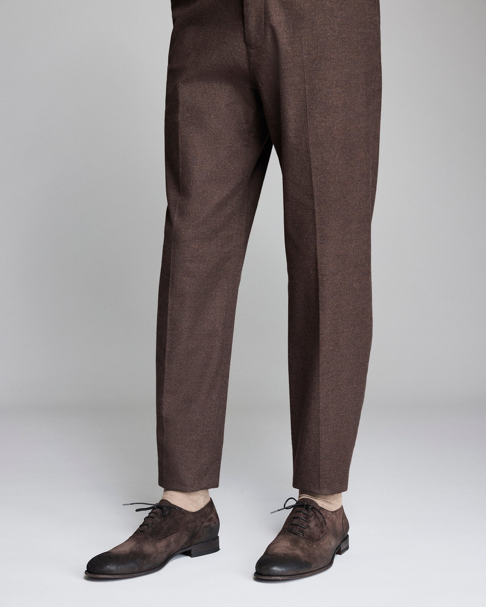 Brown dress pants worn by a person on a light gray background
