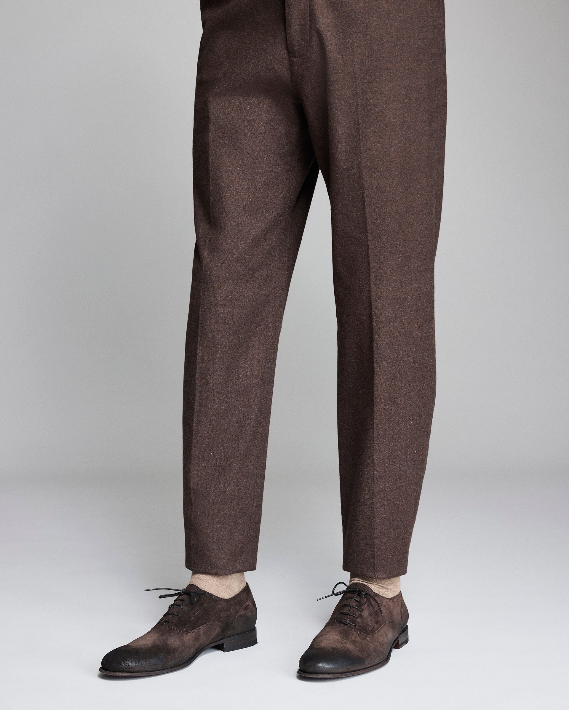 Brown dress pants worn by a person on a light gray background