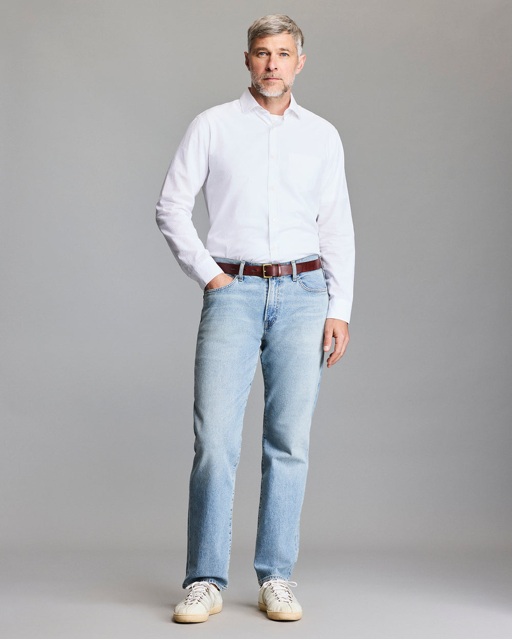 Man wearing a white shirt and light blue jeans against a gray background