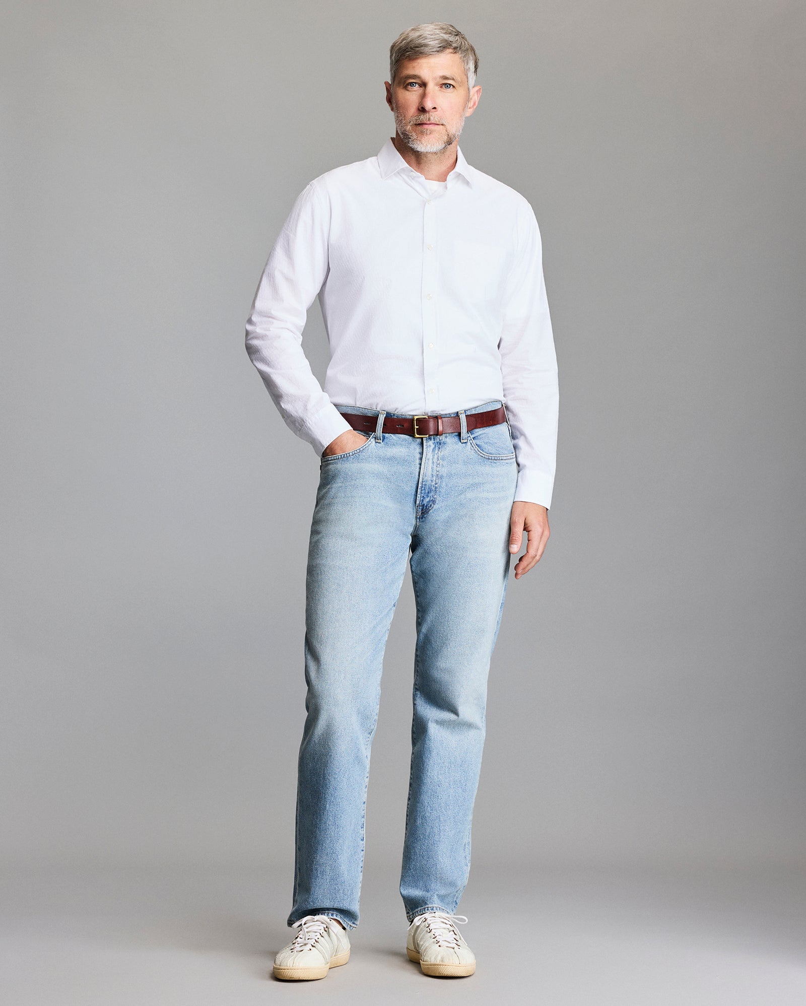 Man wearing a white shirt and light blue jeans against a gray background