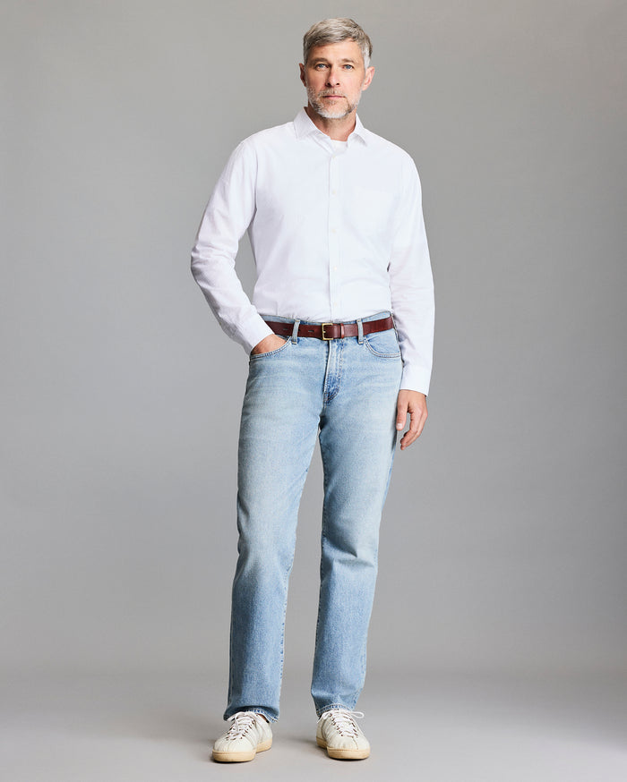 Man wearing a white shirt and light blue jeans against a gray background