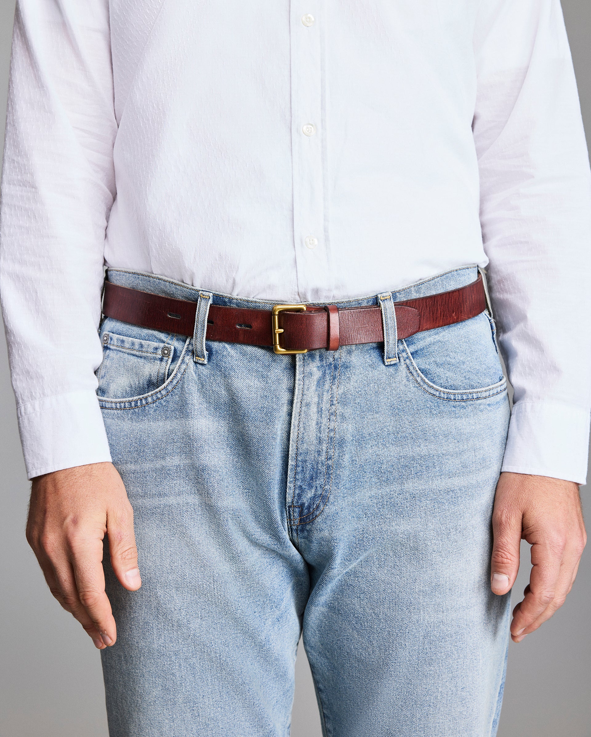 Person wearing a white shirt, light blue jeans, and a brown belt with a gold buckle.