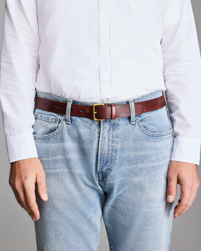 Person wearing a white shirt, light blue jeans, and a brown belt with a gold buckle.
