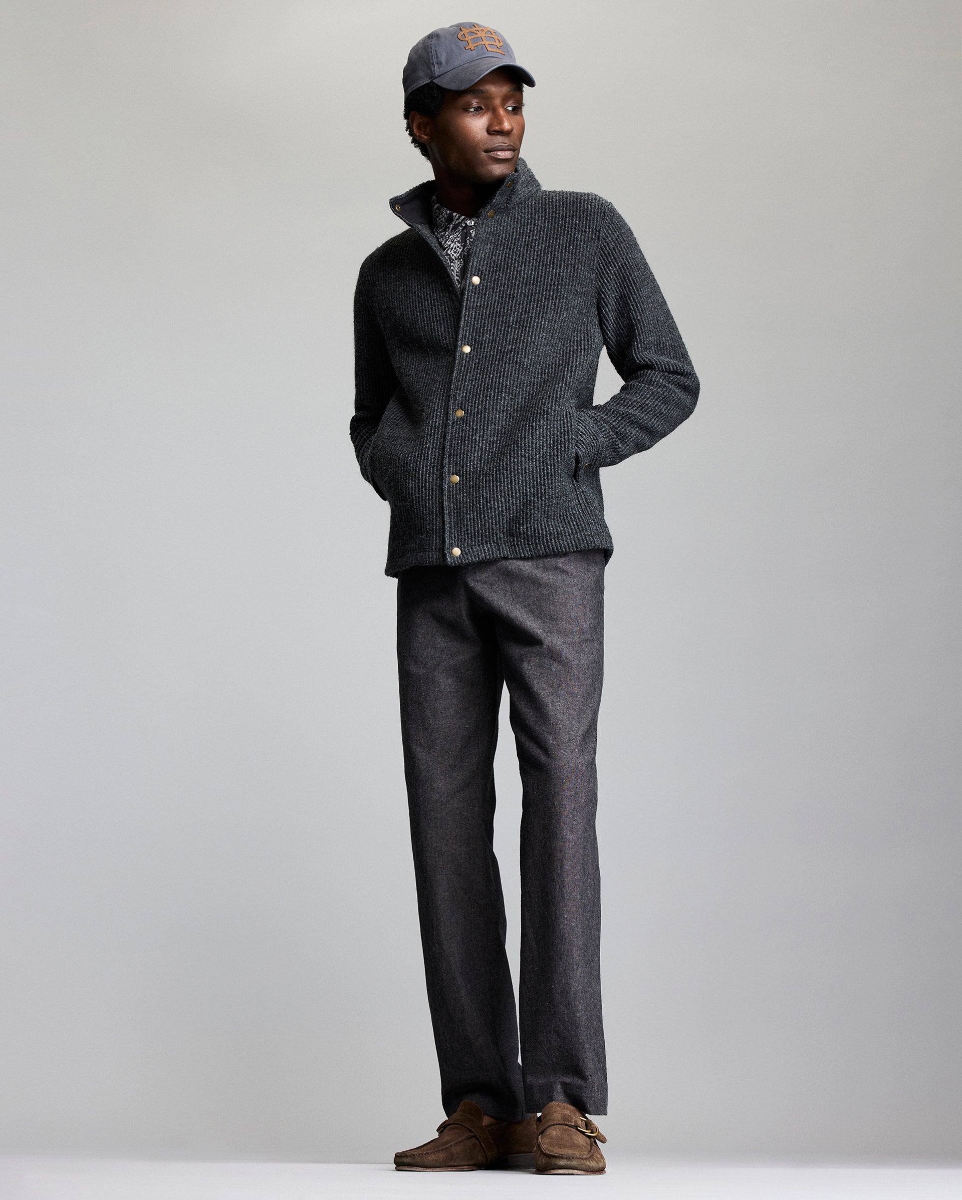 Man wearing a dark gray jacket, pants, and cap on a light gray background