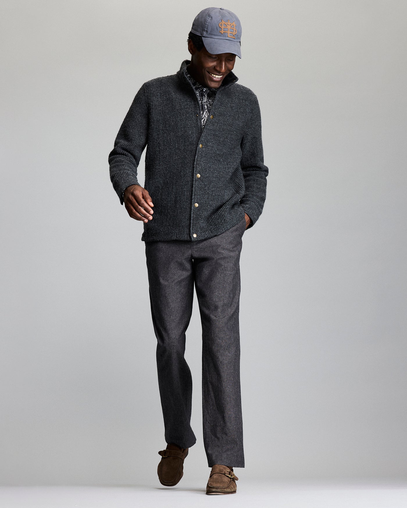 Man wearing a gray sweater, cap, and pants on a plain background