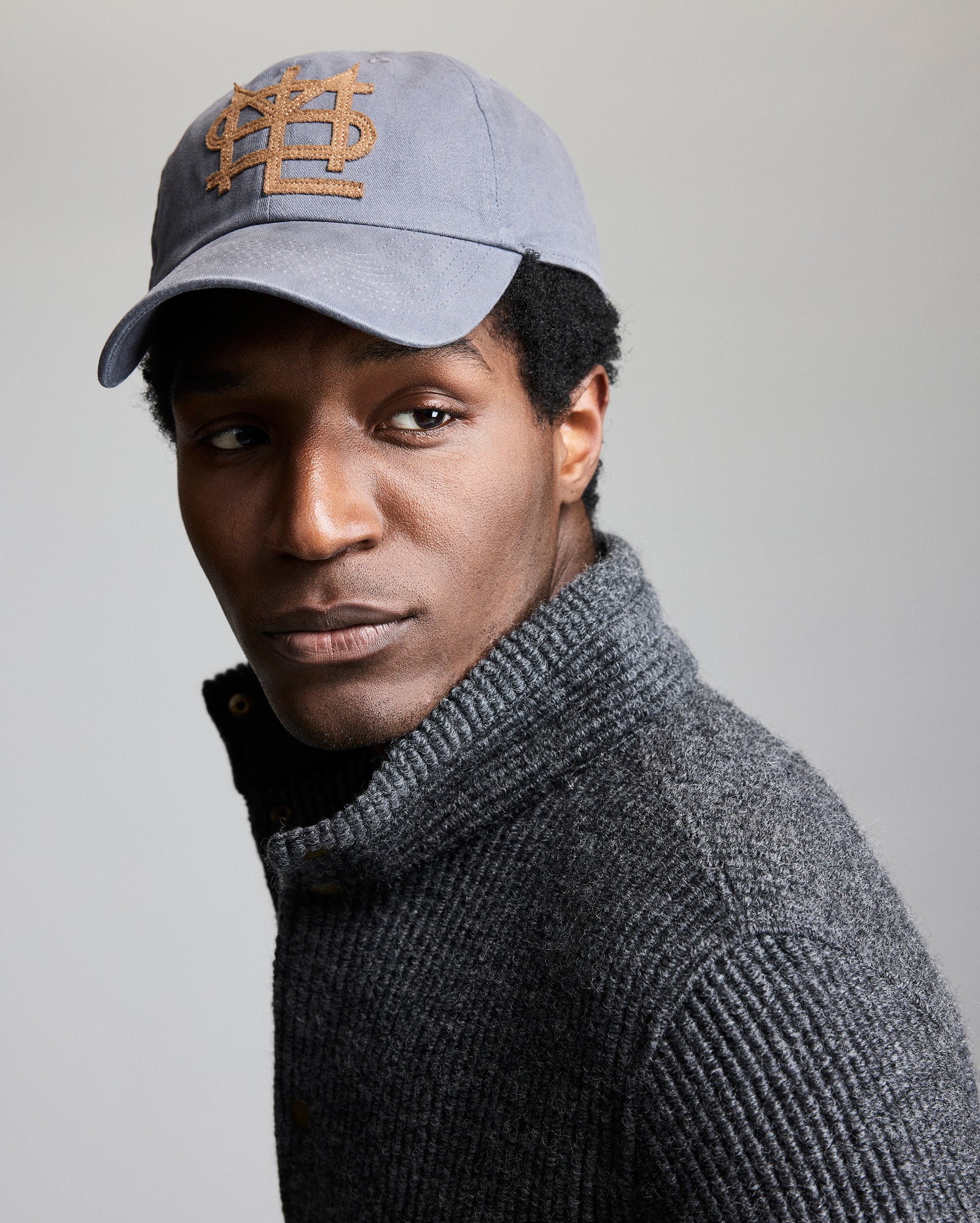 Man wearing a gray cap with a logo and a gray sweater on a plain background