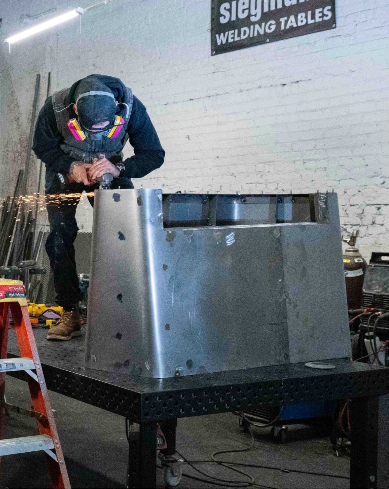 Person welding a large metal structure on a welding table with 'Siegmann' branding.