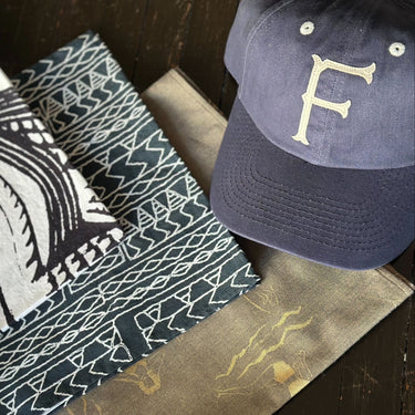 Navy cap with a gold 'F', patterned fabric, and black wallet on a wooden surface