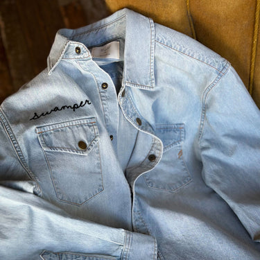 Light blue denim jacket with 'Swamper' branding on a yellow surface