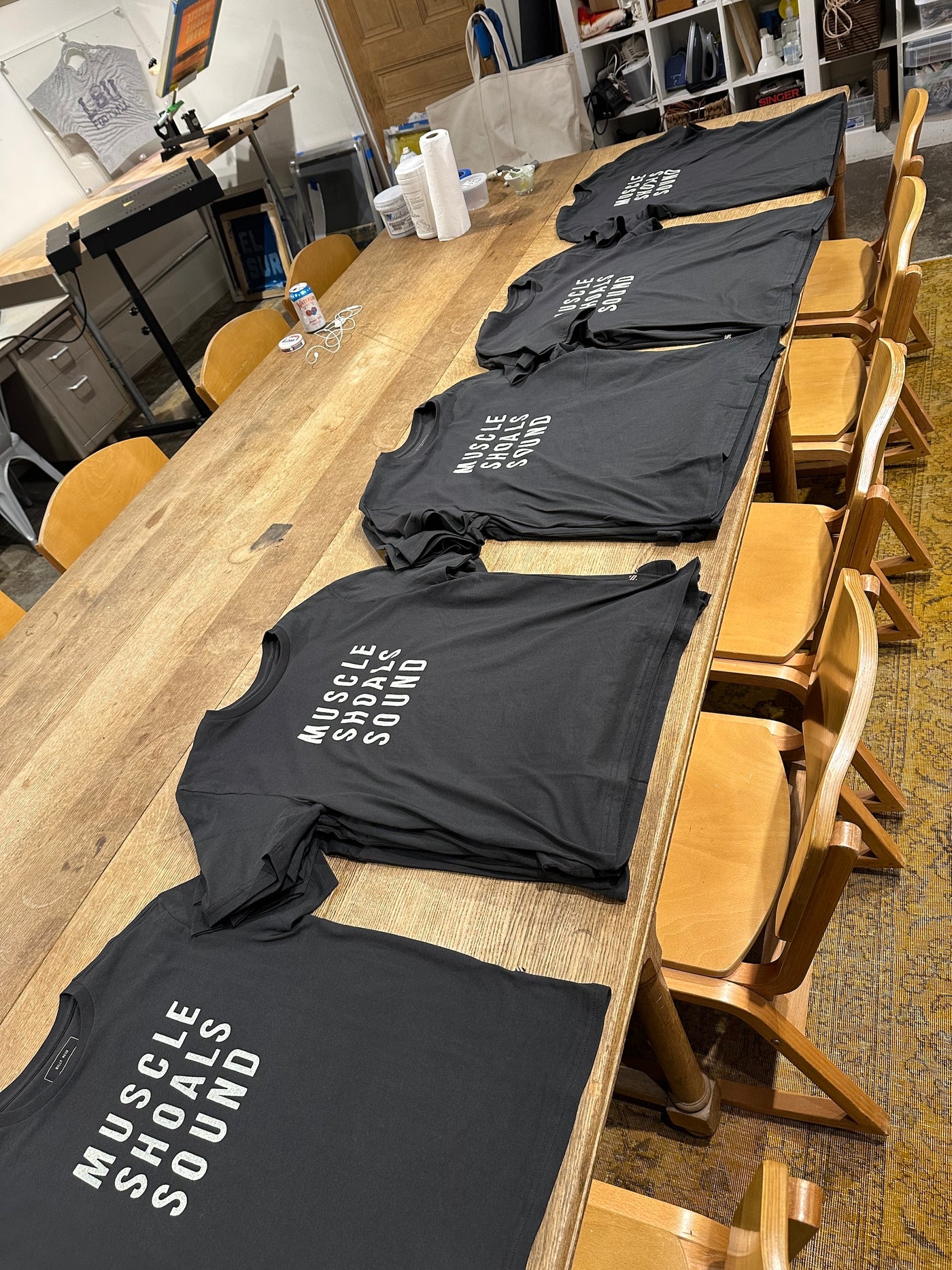 Black shirts reading 'Muscle Shoals Sound' across the chest laid out on a wooden table.