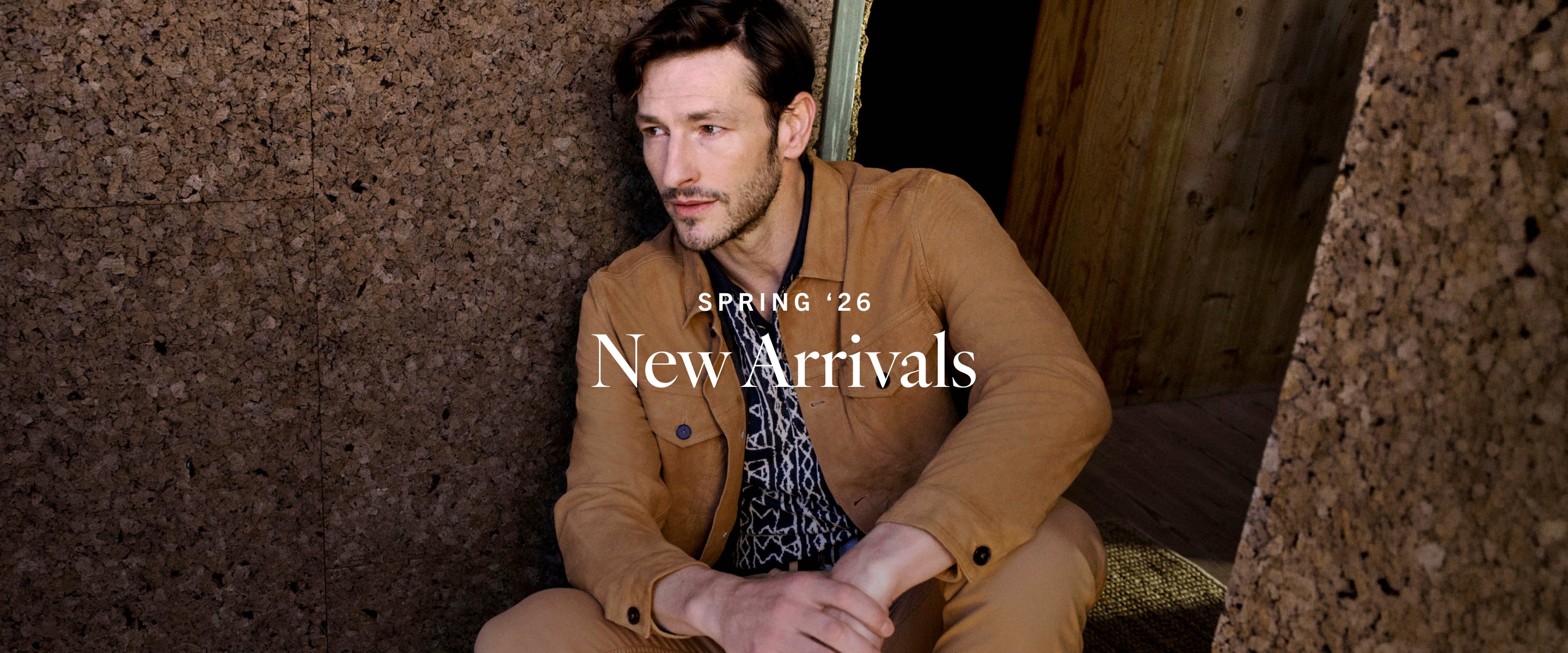 Man sitting against a textured wall with 'Spring '26 New Arrivals' text overlay.