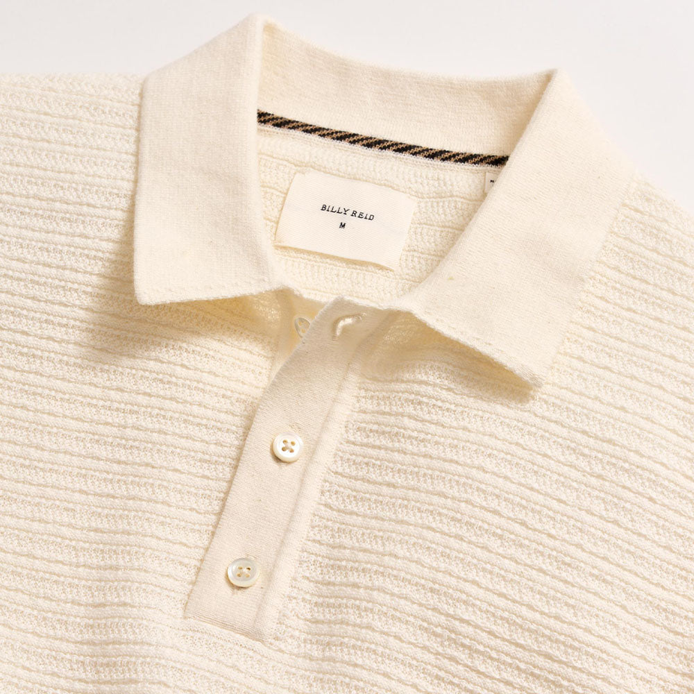 Close-up of a cream-colored knit polo shirt with a brand label on a light gray background