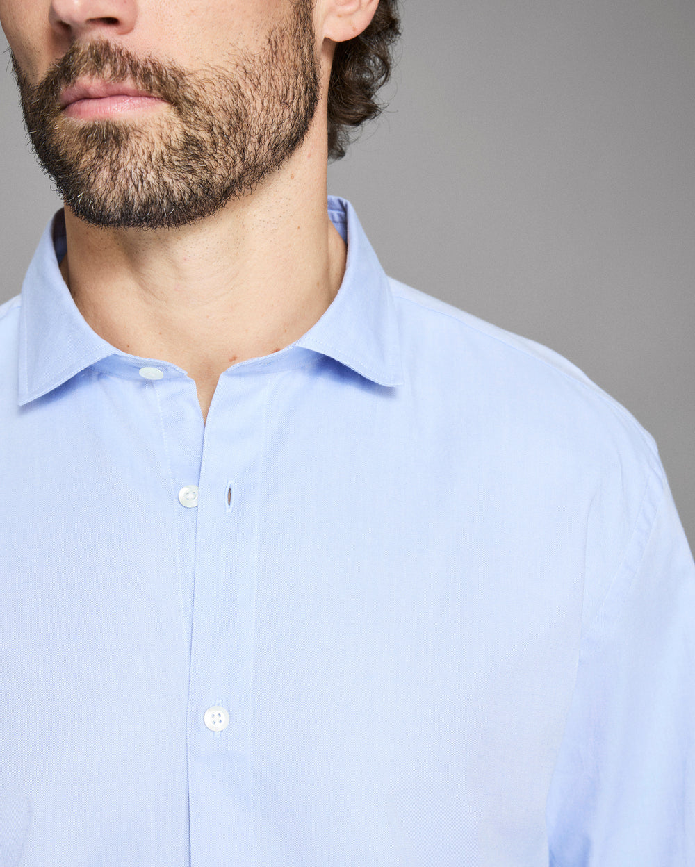Man wearing a light blue dress shirt against a gray background