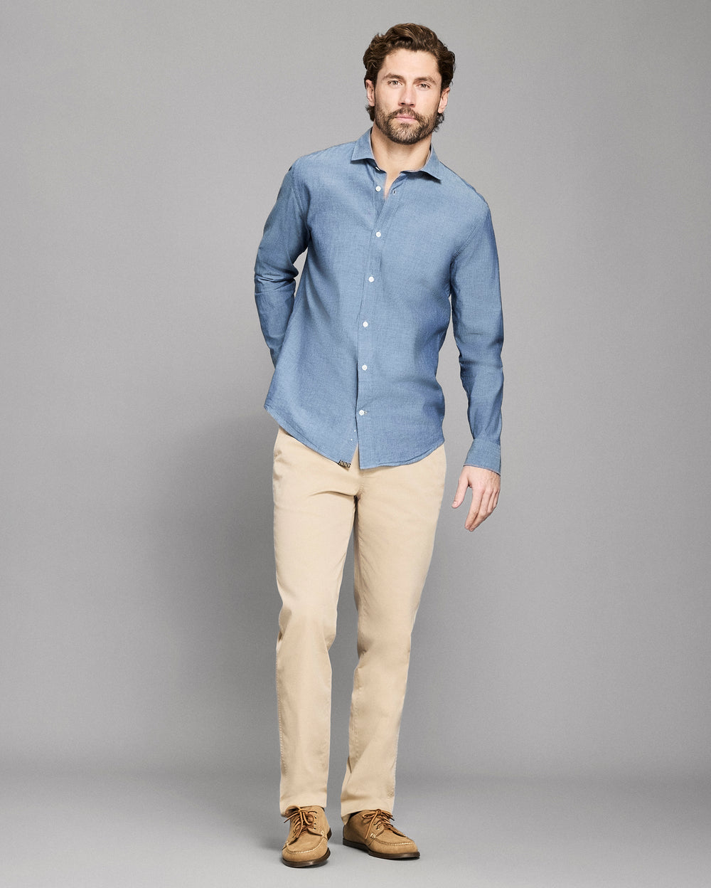 Man wearing a blue shirt and beige pants against a gray background