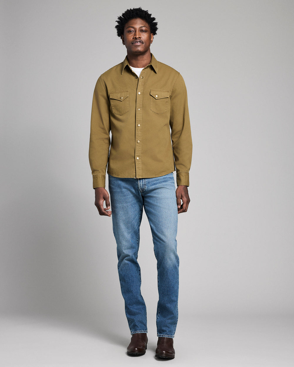 Man wearing a green shirt and blue jeans against a gray background