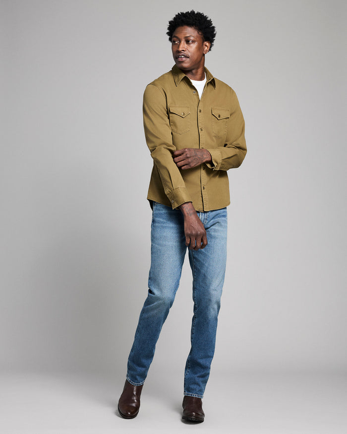 Man wearing a mustard yellow shirt and blue jeans on a gray background