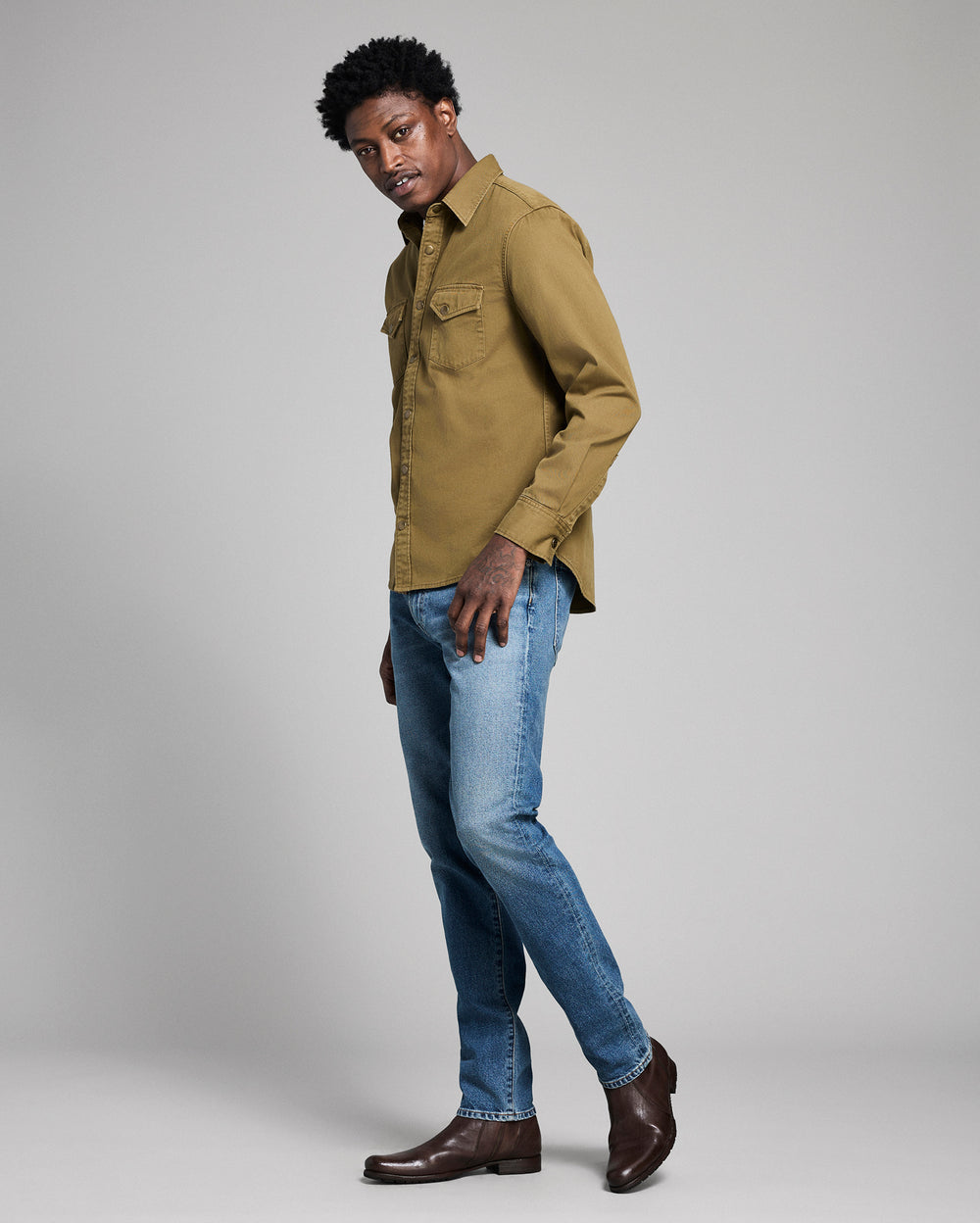 Man wearing a green shirt and blue jeans on a gray background