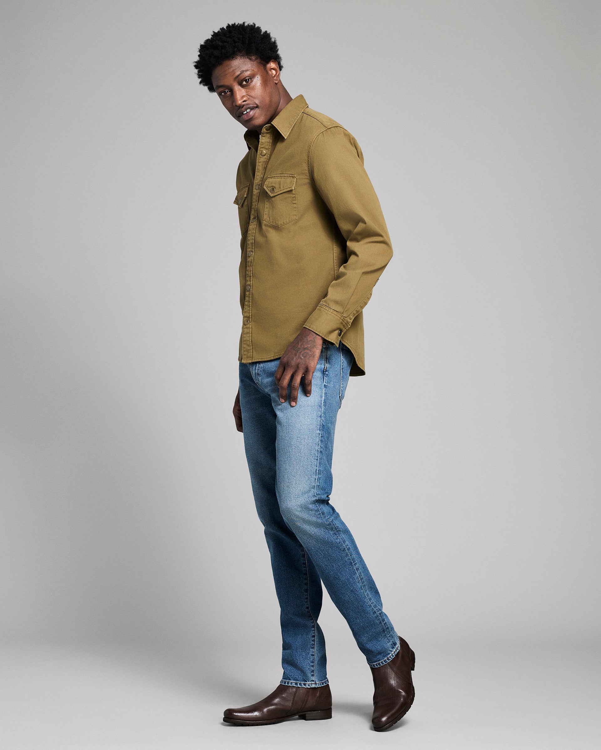 Man wearing a green shirt and blue jeans on a gray background