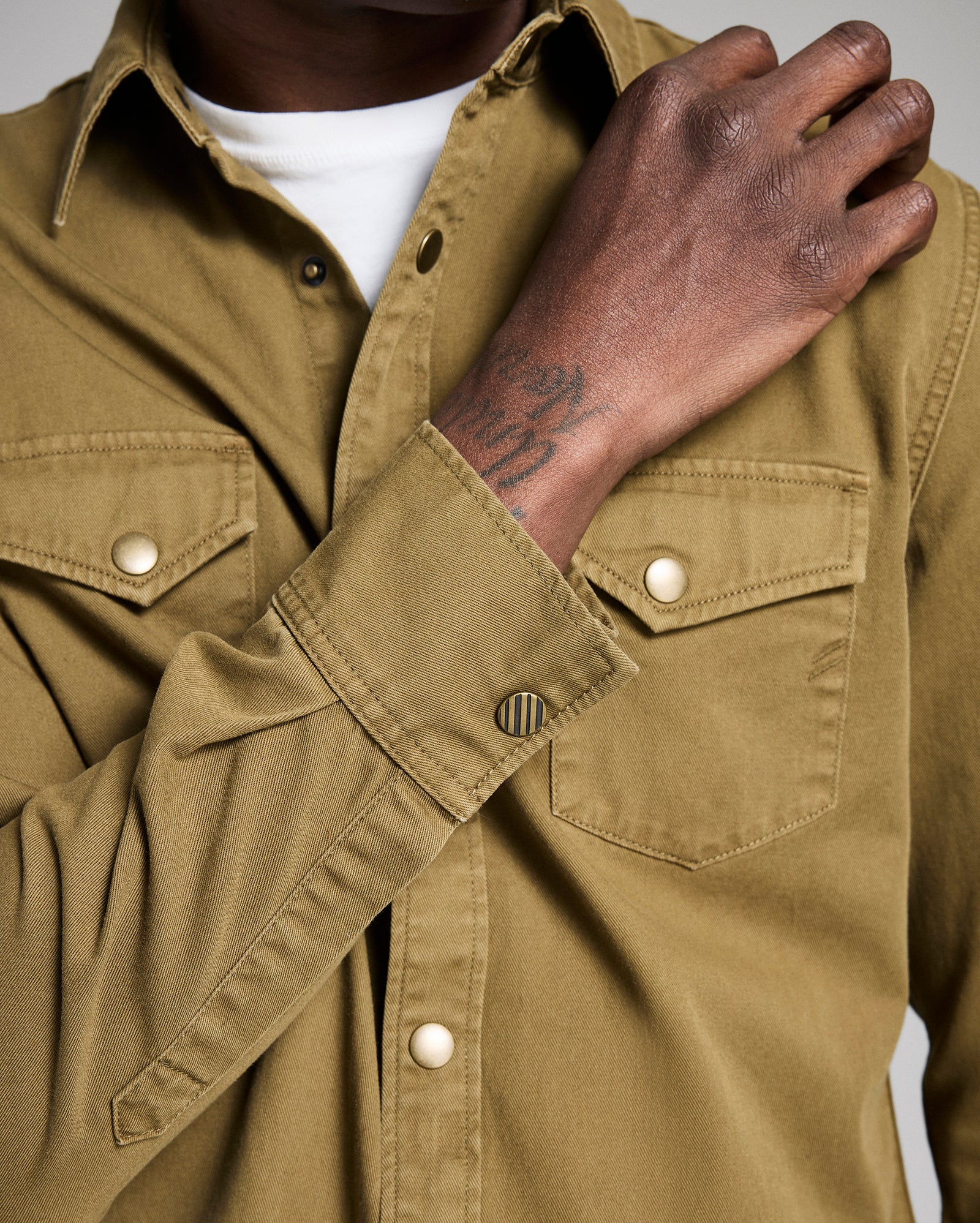 Close-up of a person wearing a brown shirt with a visible brand logo.