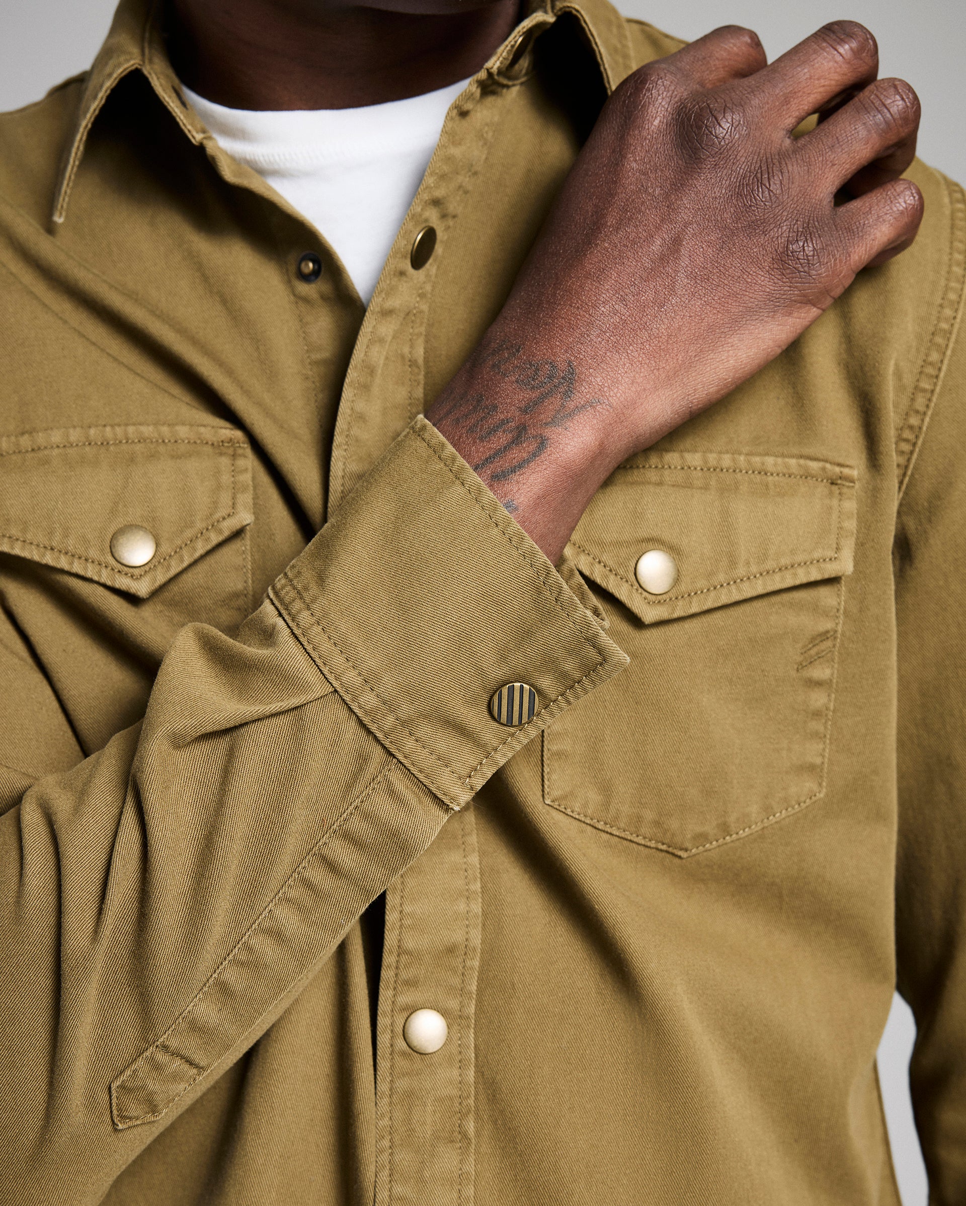 Close-up of a person wearing a brown shirt with a visible brand logo.