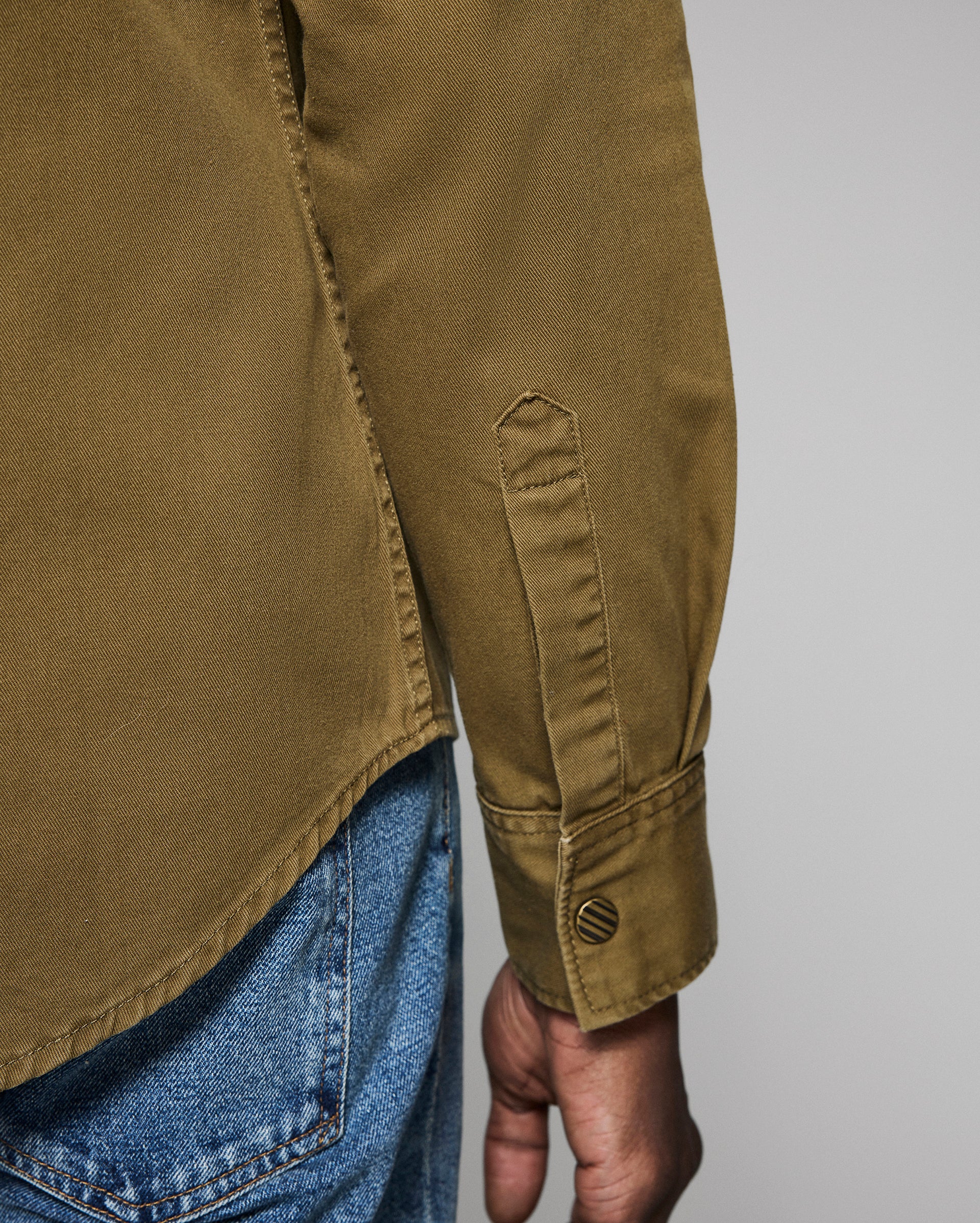 Close-up of a person wearing a green jacket with rolled-up sleeve and blue jeans on a gray background