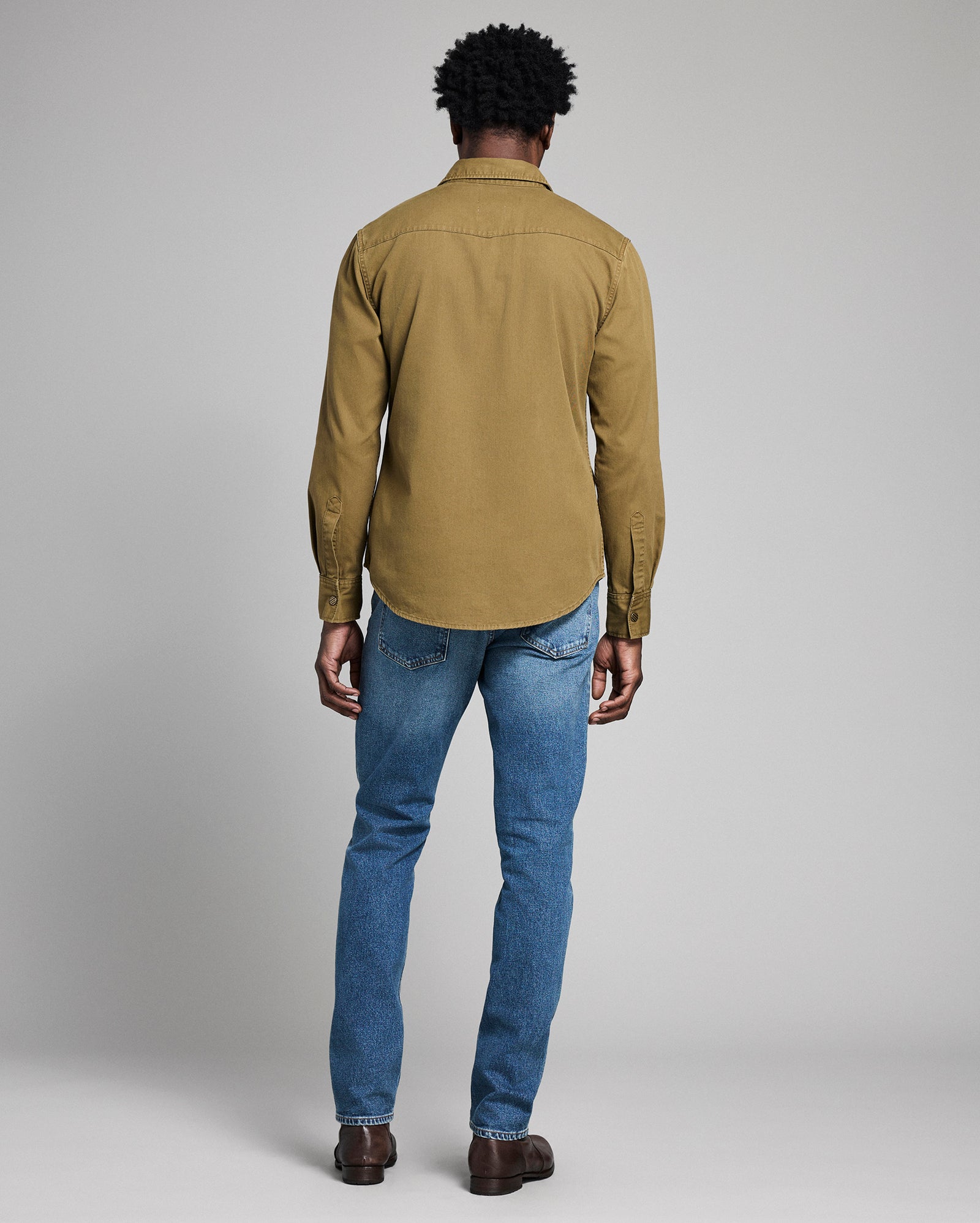 Person wearing a green shirt and blue jeans on a plain background