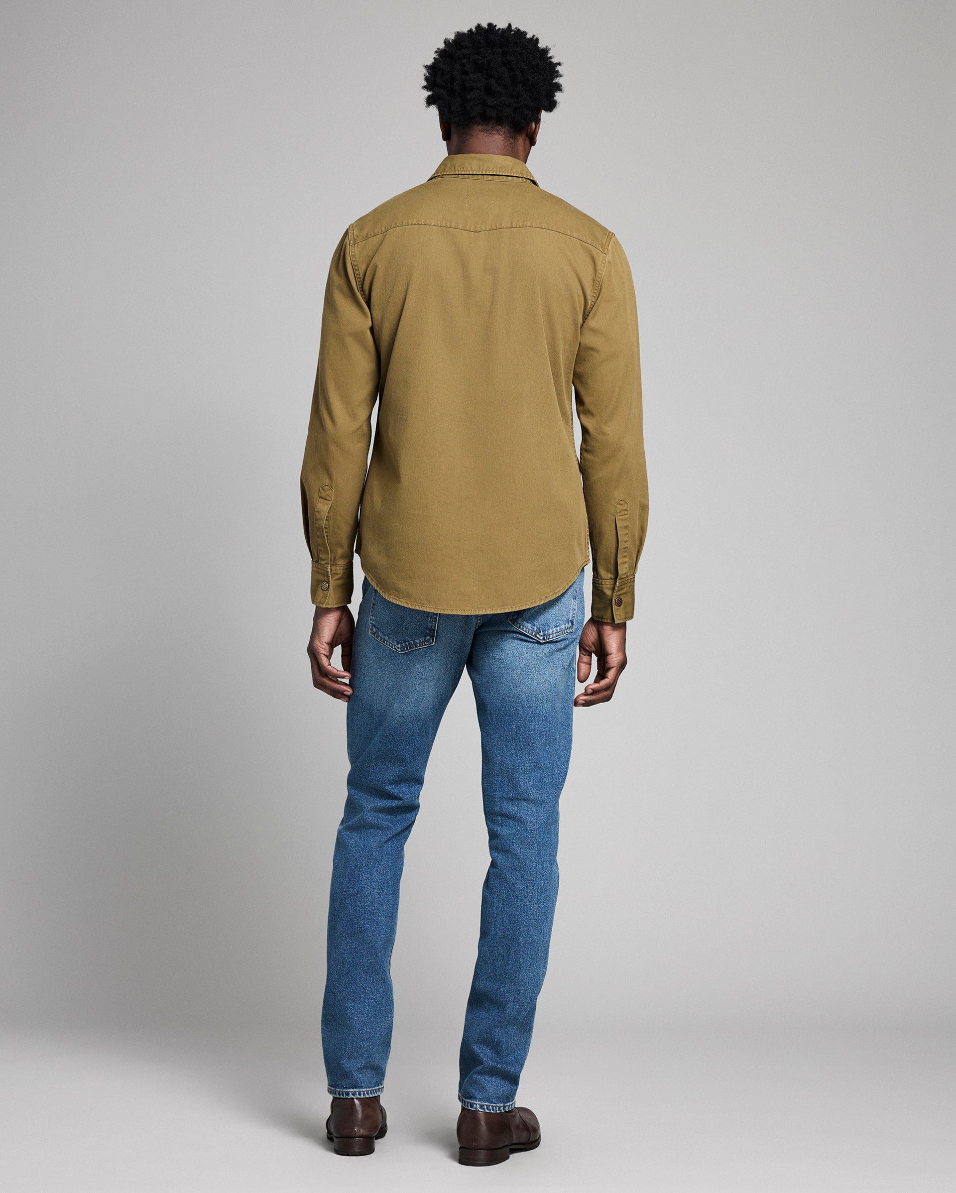 Person wearing a green shirt and blue jeans on a plain background