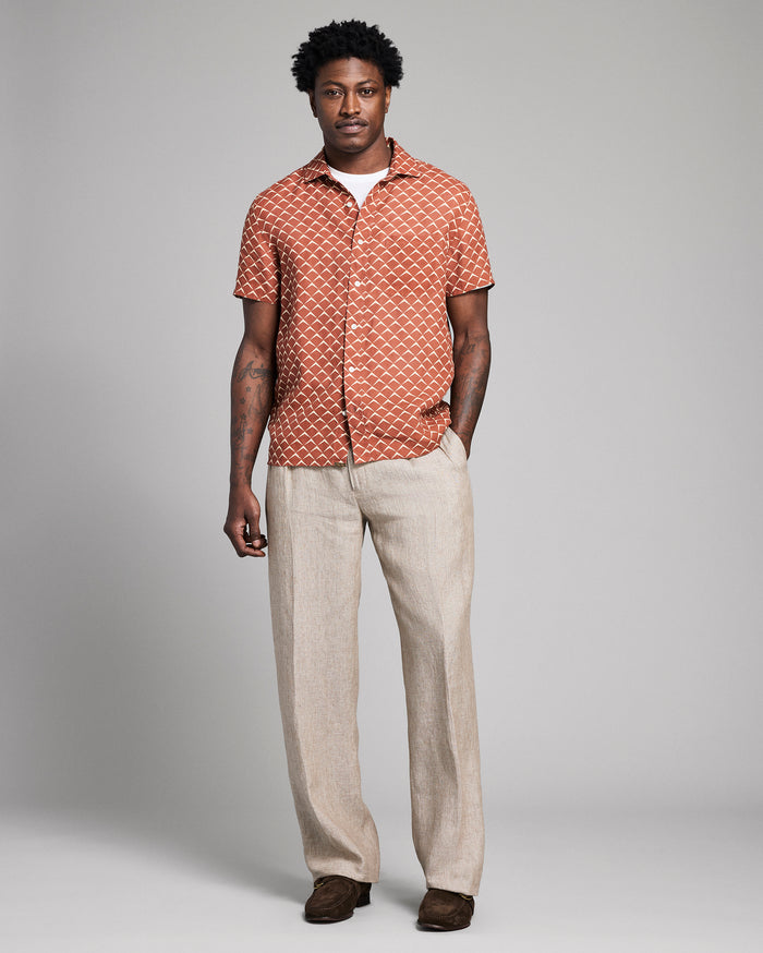 Man wearing a patterned shirt and beige pants against a gray background