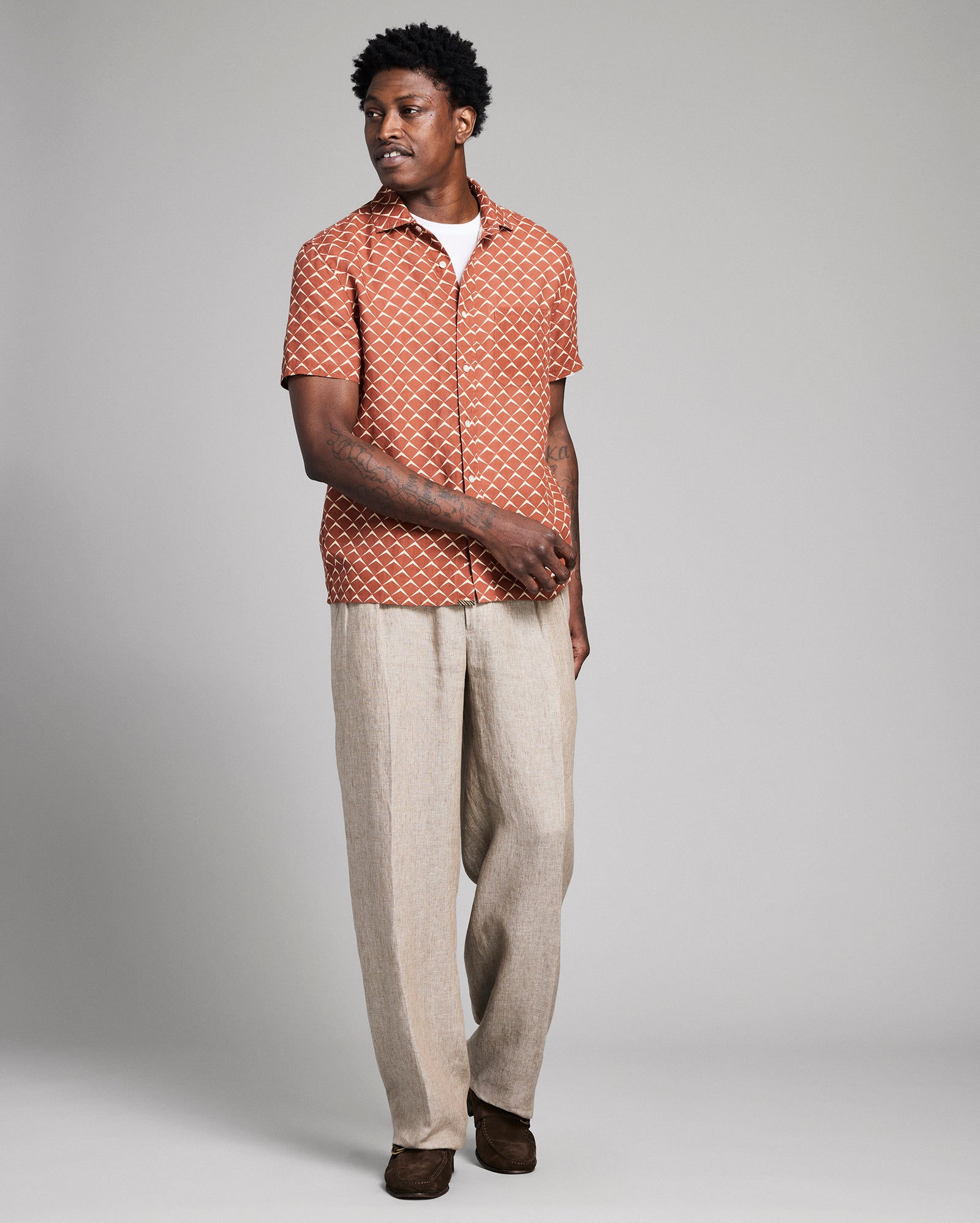 Man wearing a patterned shirt and beige pants on a gray background