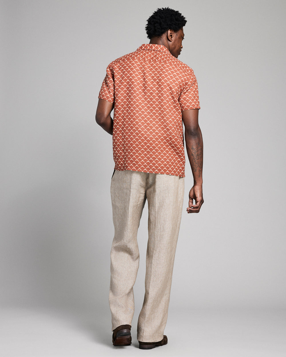 Man wearing a patterned shirt and beige pants on a plain background