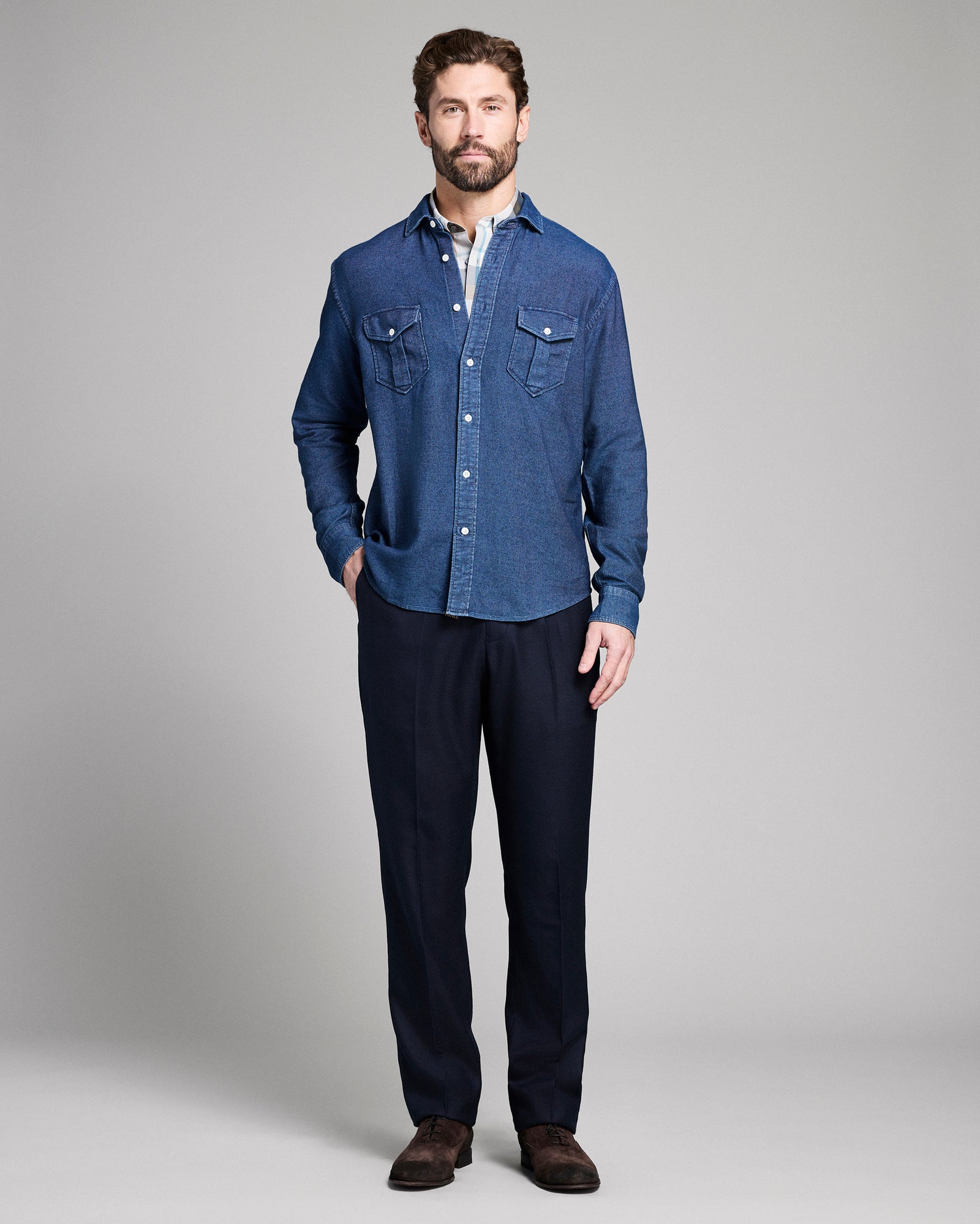 Man wearing a blue denim shirt and dark pants on a gray background