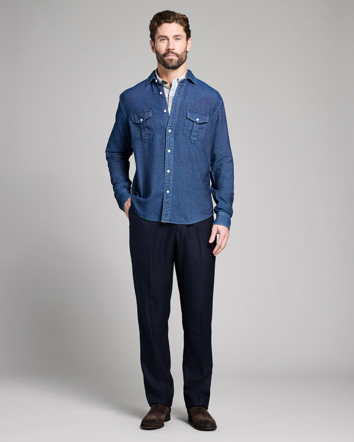 Man wearing a blue denim shirt and dark pants on a gray background