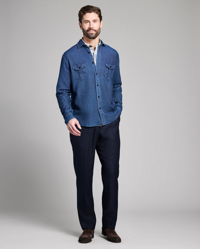 Man wearing a blue denim shirt and dark pants on a gray background Alternate