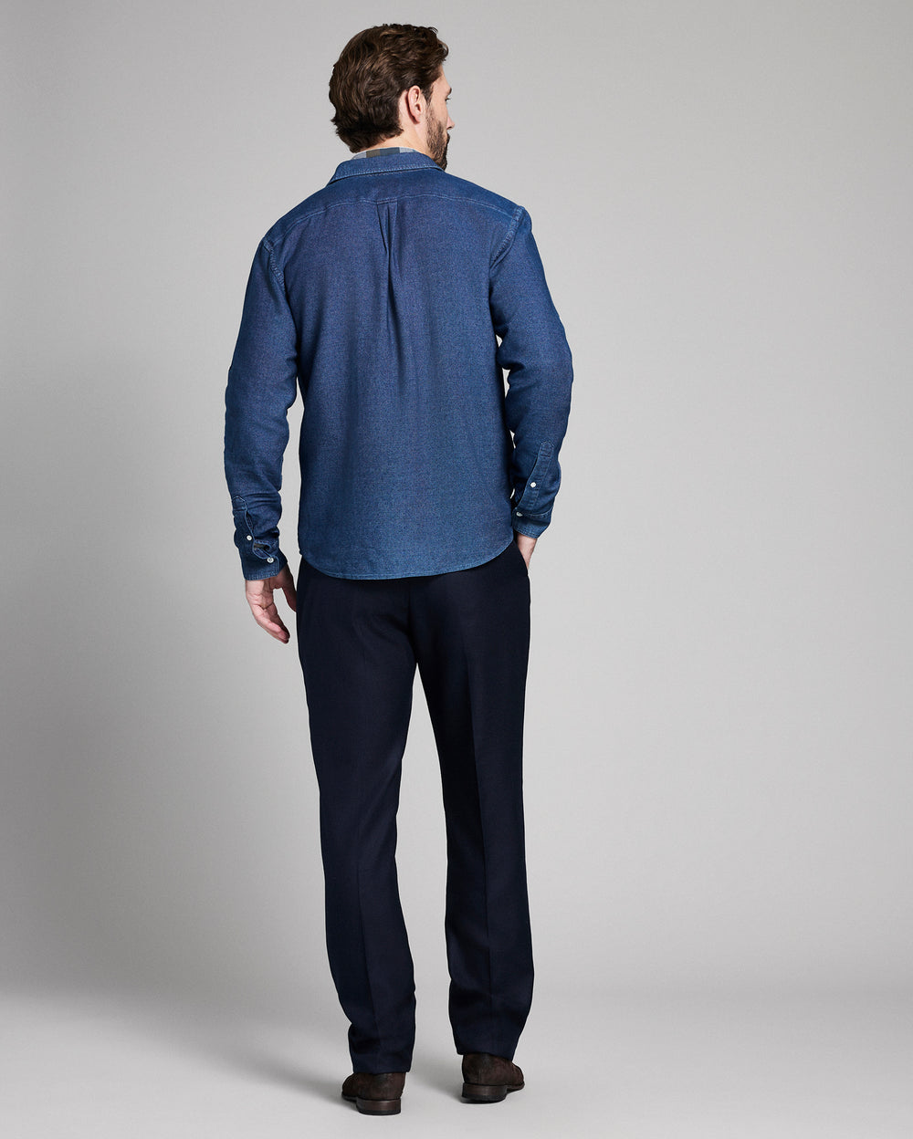 Man wearing a blue denim shirt and dark pants on a gray background