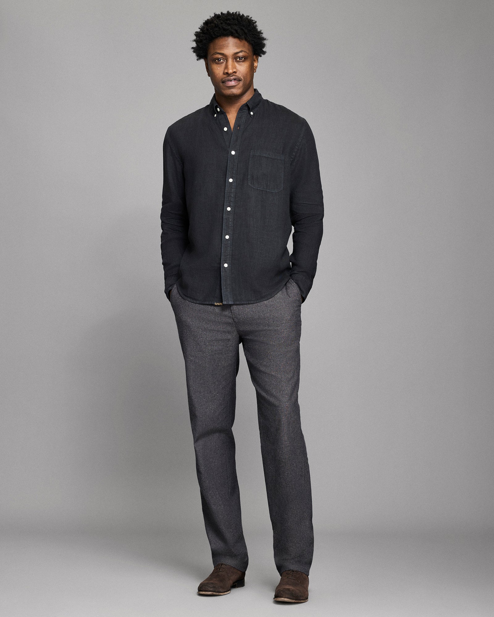 Man wearing a dark gray button-up shirt and pants against a plain background