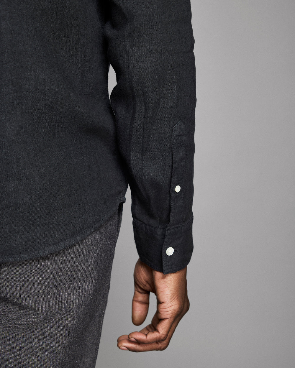 Close-up of a person wearing a black shirt with button details on a gray background