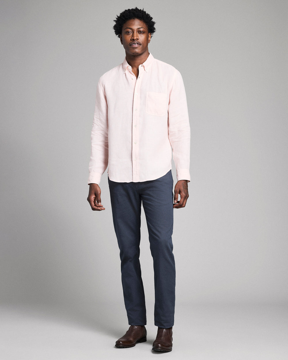 Man wearing a light pink shirt and dark blue pants on a gray background