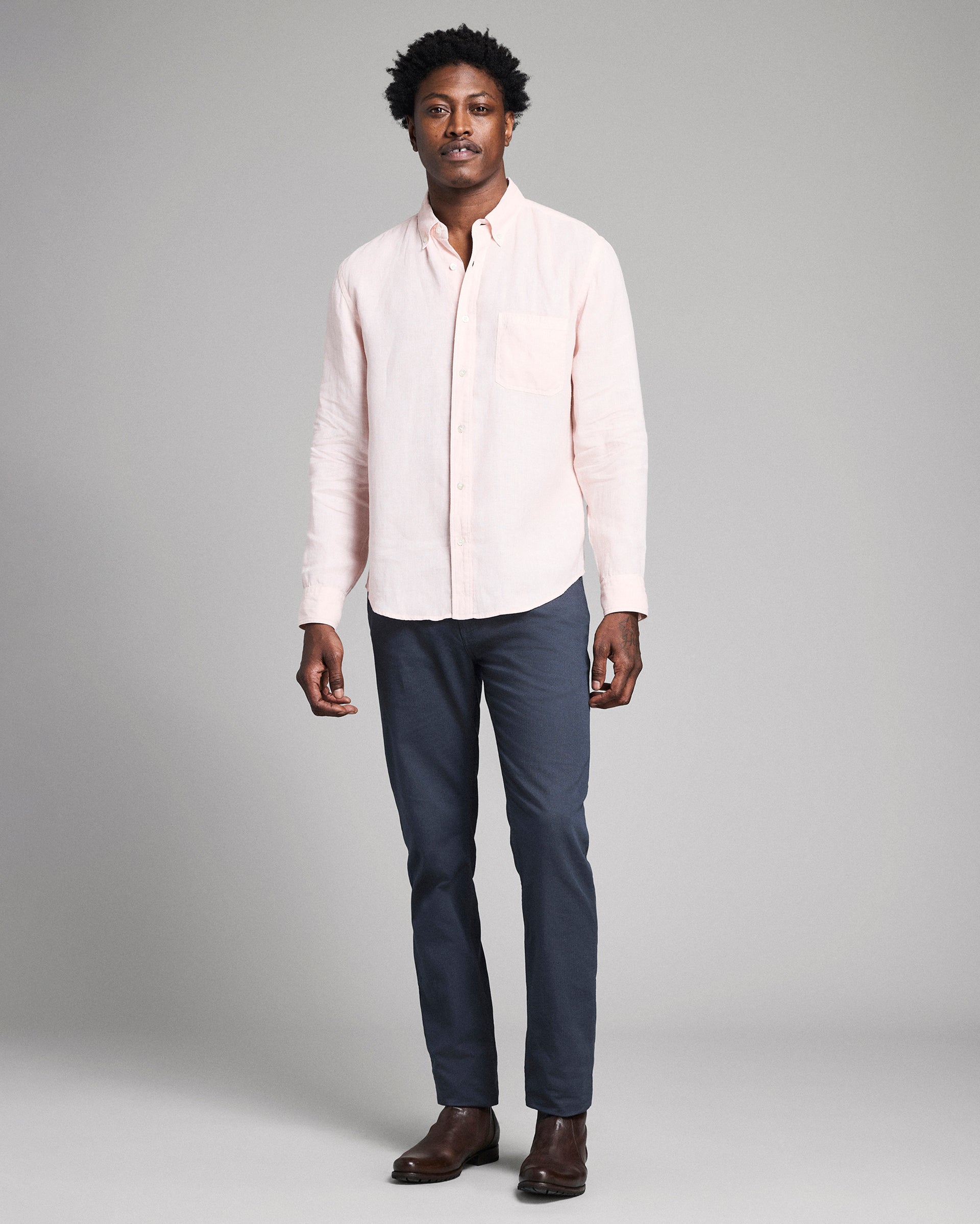 Man wearing a light pink shirt and dark blue pants on a gray background