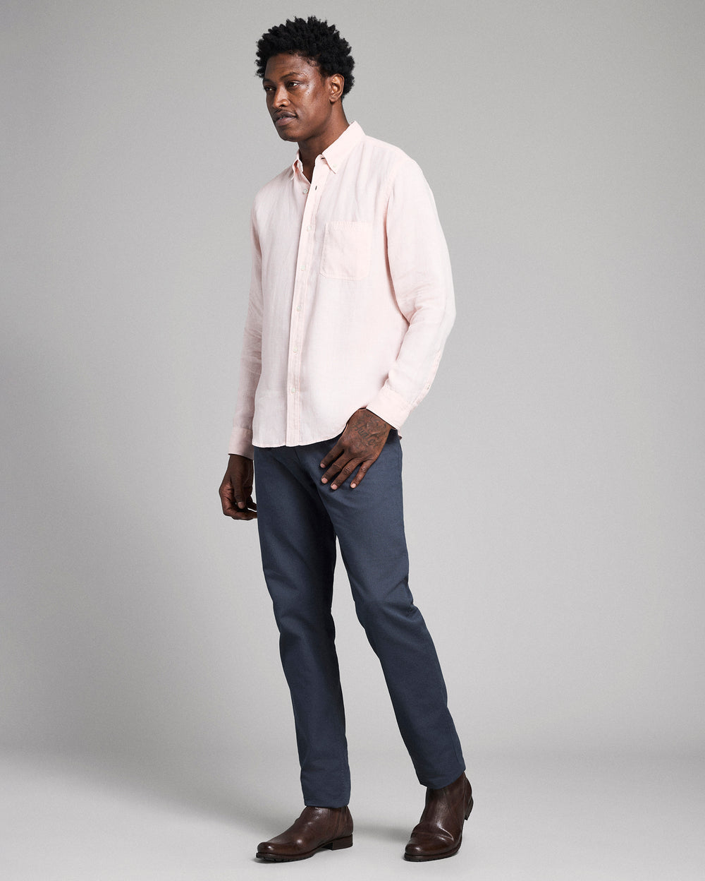 Man wearing a light pink shirt and dark blue pants on a gray background