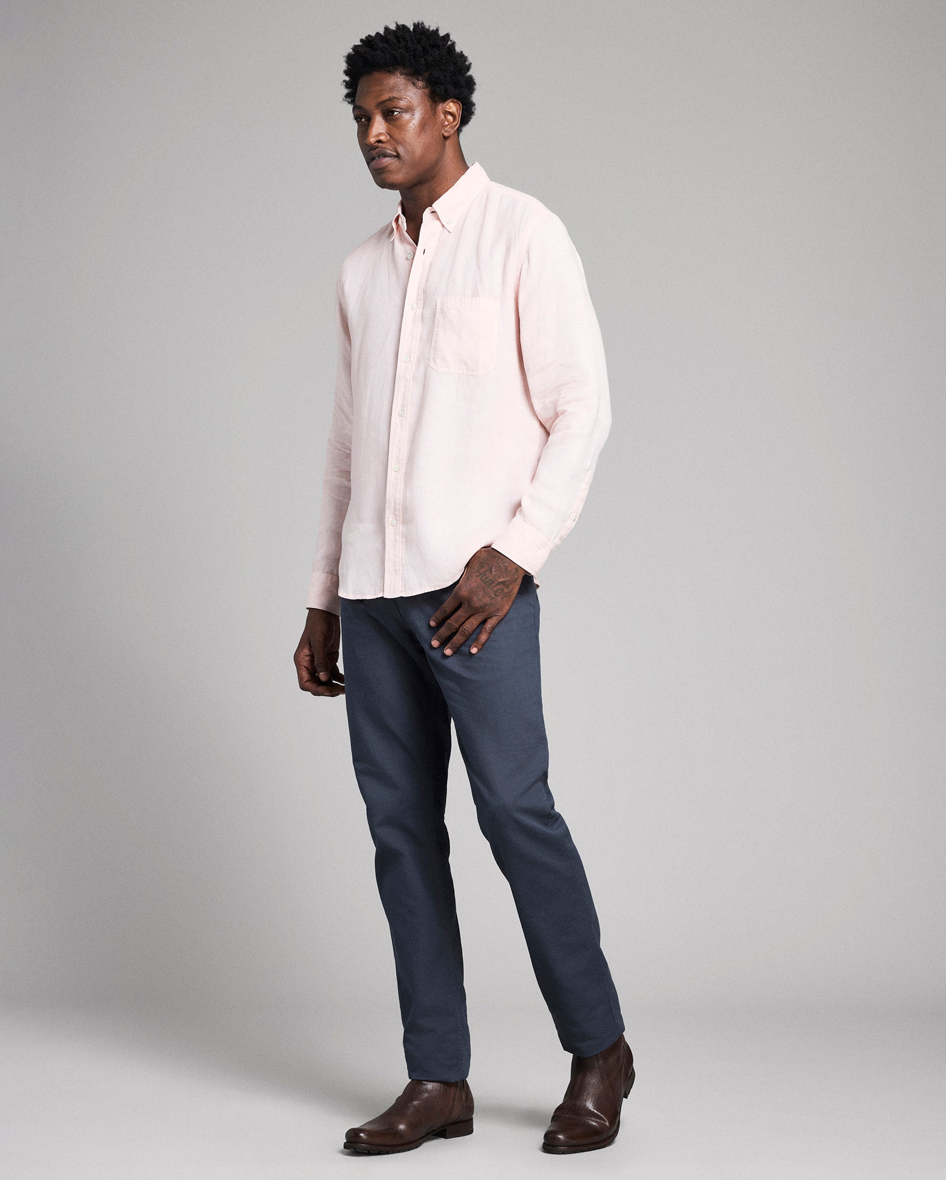 Man wearing a light pink shirt and dark blue pants on a gray background