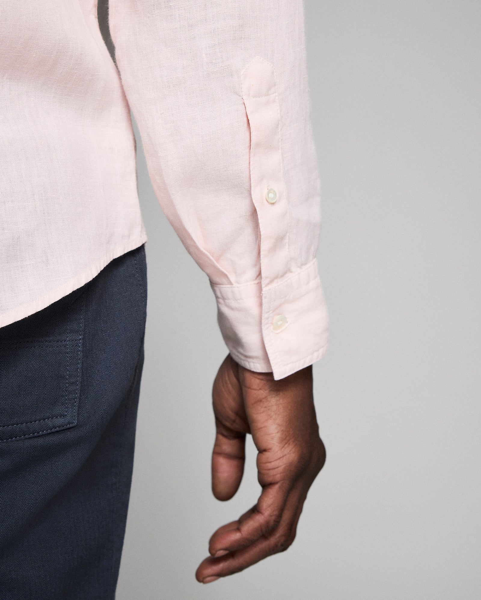Person wearing a light pink shirt with rolled-up sleeves against a gray background
